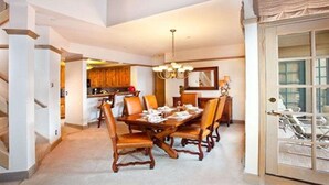 A dining area with a wooden table and chairs, a chandelier, and a view of the kitchen in the background. - LUXURIOUS AND SPACIOUS CONDO ,SKI IN/ SKI OUT IN BEAVER CREEK, COLORADO. (Avon)