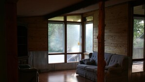 Una habitación con paredes de madera, un sofá a cuadros, una silla y ventanas amplias con vistas al exterior.