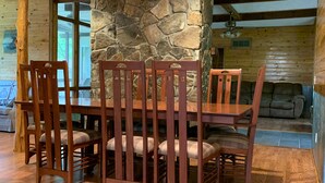 Una mesa de madera para comer con seis sillas, un pilar de piedra y un techo de madera con vigas a la vista.