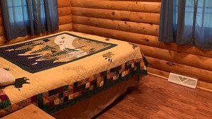 Una habitación tipo cabaña de madera con una cama, un colcha y cortinas.