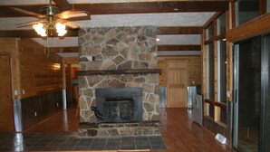 Un hall amplio con chimenea de piedra, piso de madera y grandes ventanales.