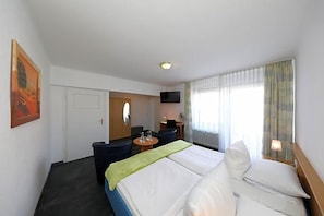 A hotel room with a bed, a desk, a chair, a television, and a window with curtains.