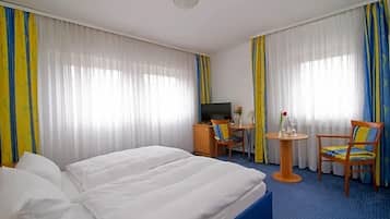 Ein Hotelzimmer mit Bett, Schreibtisch, Sessel und Fernseher.