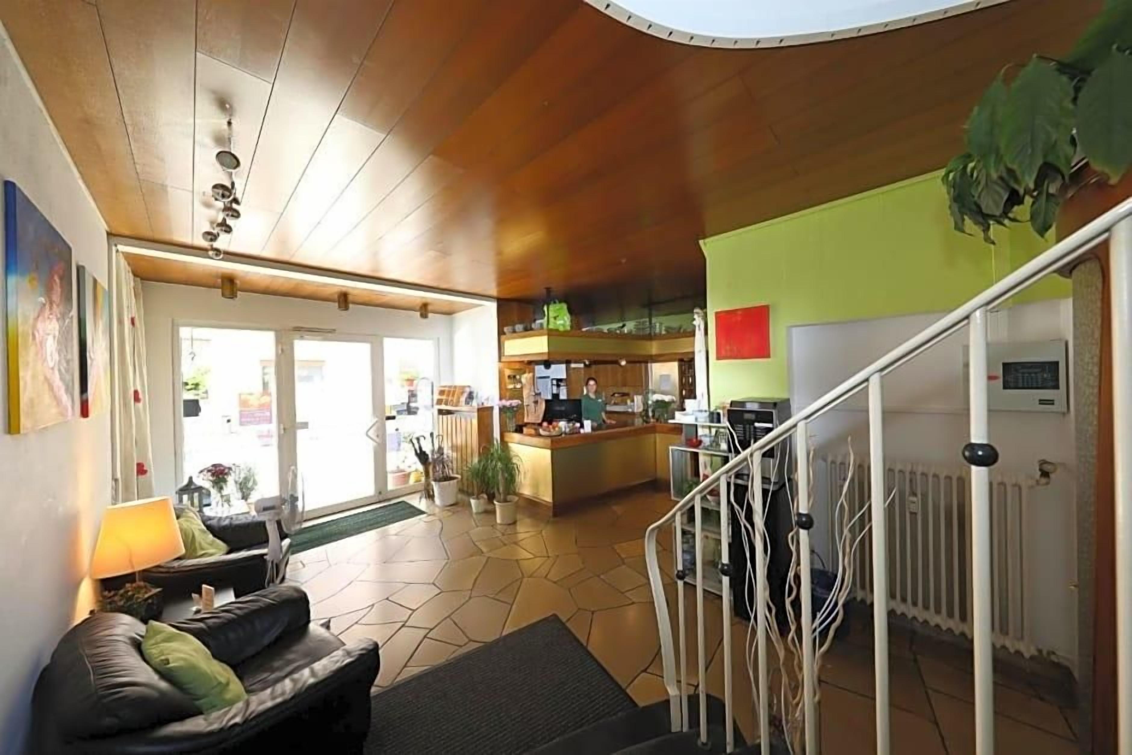 Eine Hotelhalle mit einer Rezeption, einer Treppe und einer Sitzecke mit Sofa und Lampe.