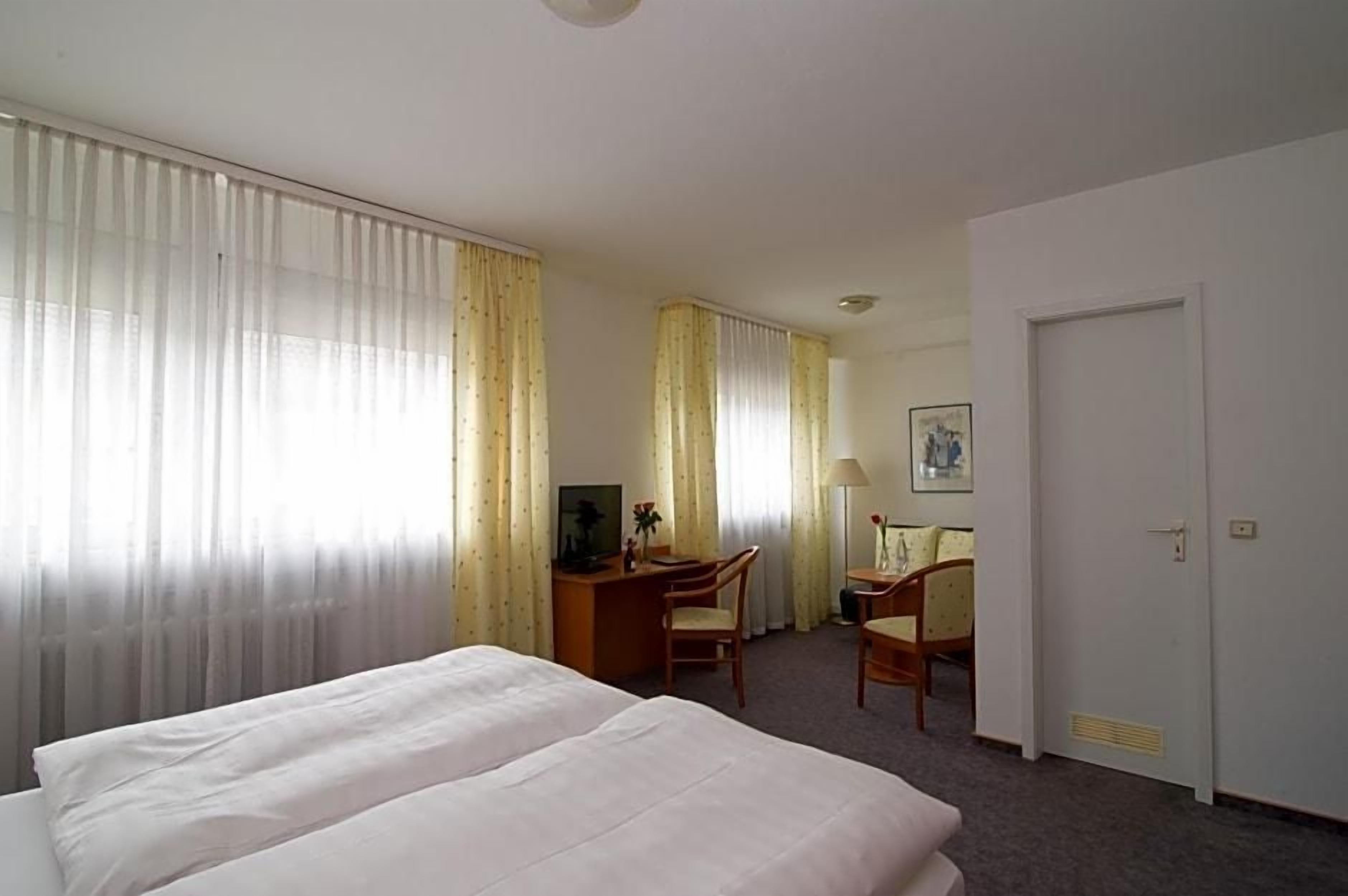 Ein Hotelzimmer mit einem Bett, einem Schreibtisch, zwei Stühlen und einer Tür.