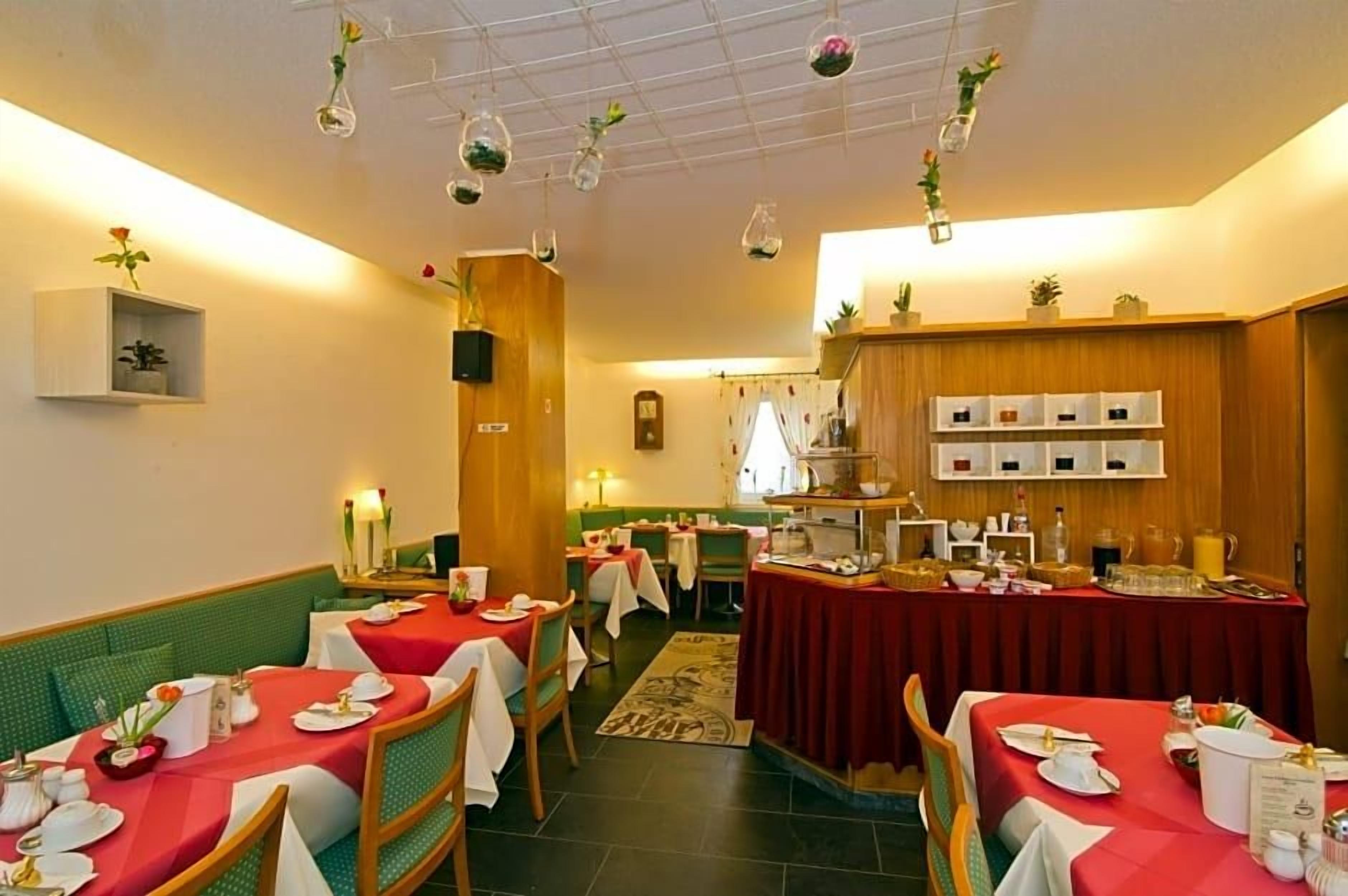 Un comedor con mesas dispuestas para comidas, un bufé con diversas opciones de alimentos y plantas colgantes.
