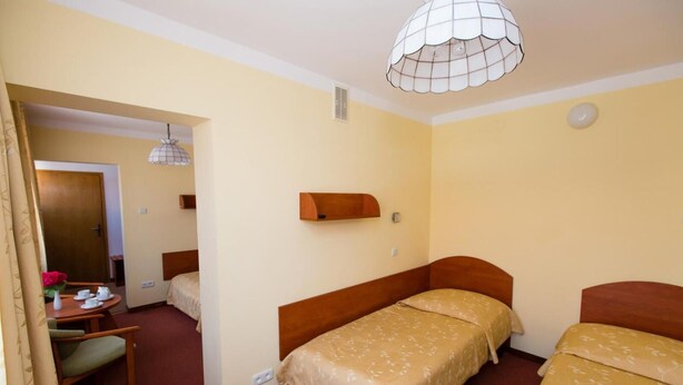 A hotel room with two single beds, a small desk with a chair, a hanging light fixture, and a door leading to another room. - Geovita Zlockie (Muszyna)