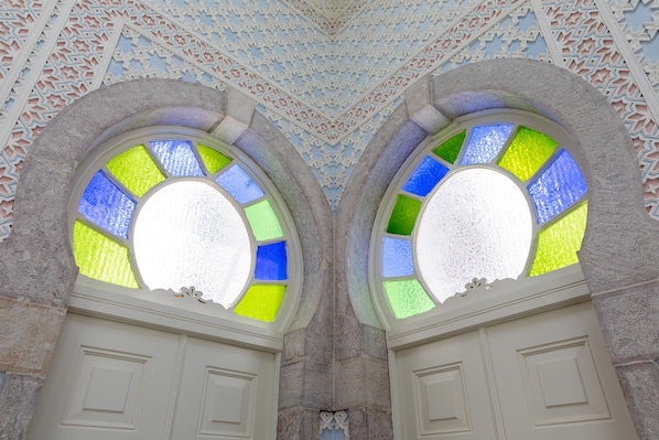Zwei gewölbte Fenster mit farbigem Buntglas, eingelassen in eine Steinwand mit aufwendigen Schnitzereien.