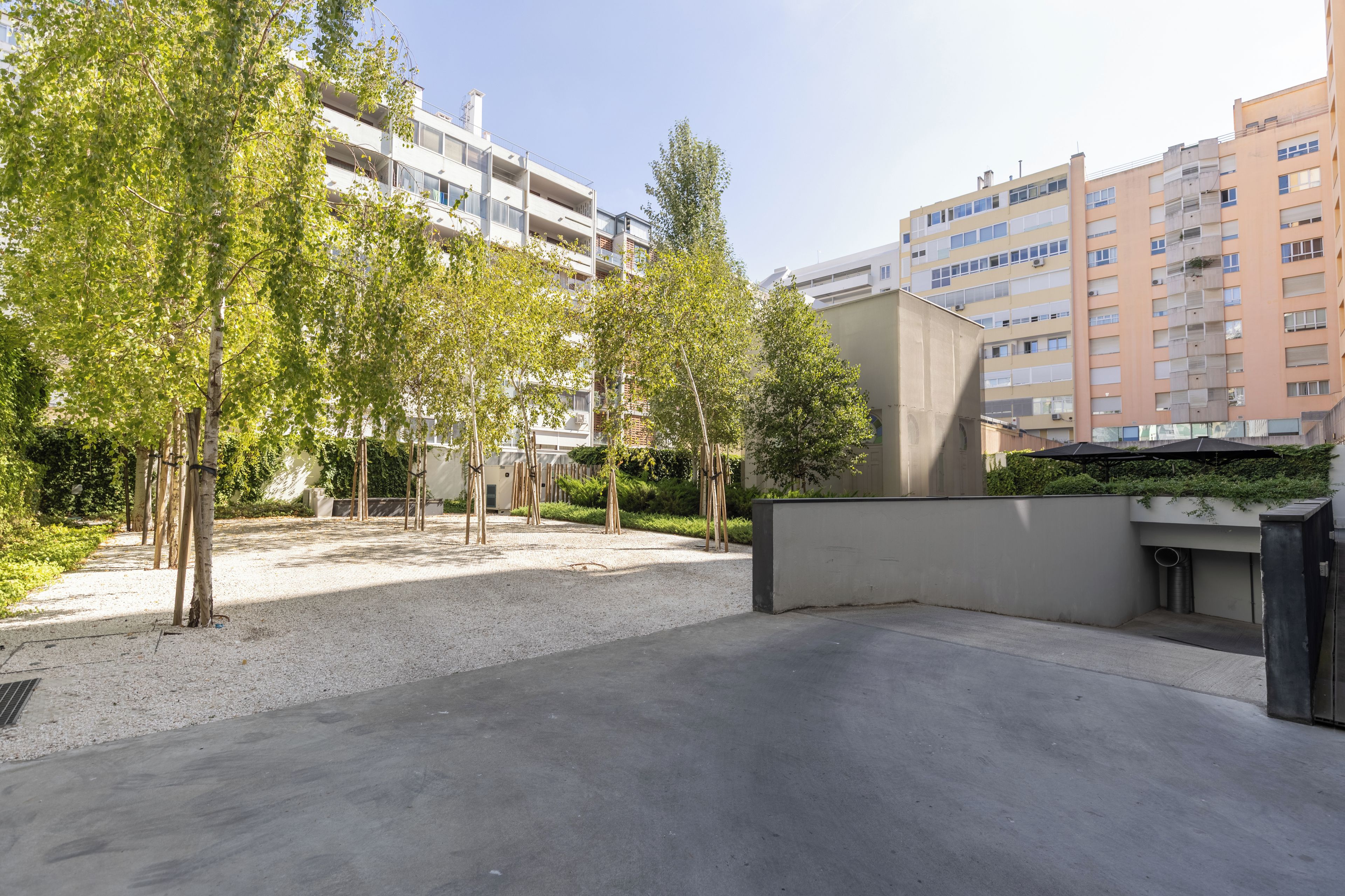 A courtyard with trees, a gravel path, and modern buildings in the background.