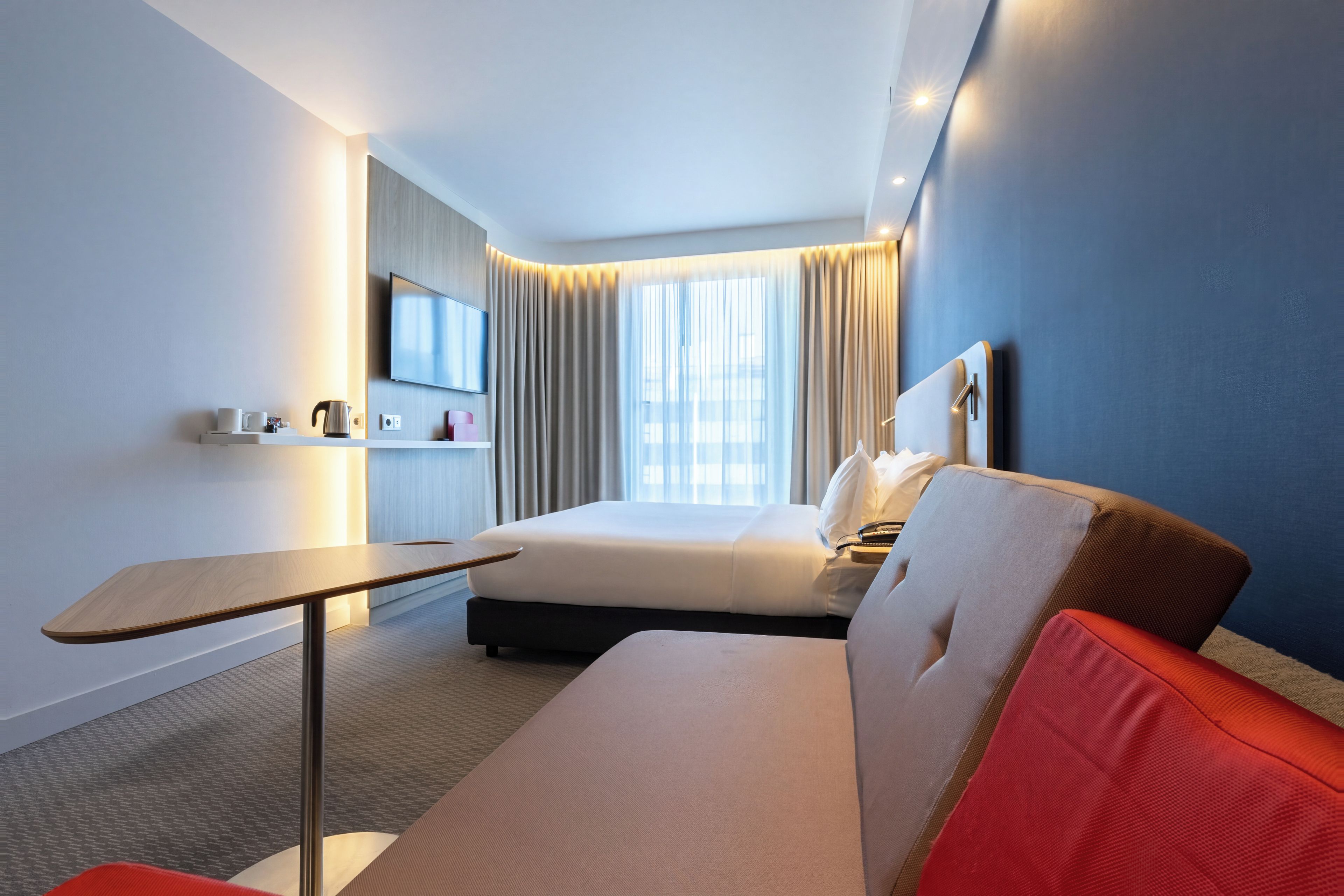 Una habitación de hotel moderna con una cama, un escritorio, un televisor de pantalla plana y un gran ventanal con cortinas.