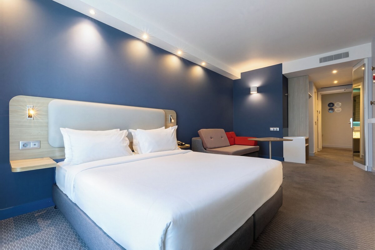 Une chambre d’hôtel moderne avec un grand lit, une table de chevet, une chaise et une petite table.