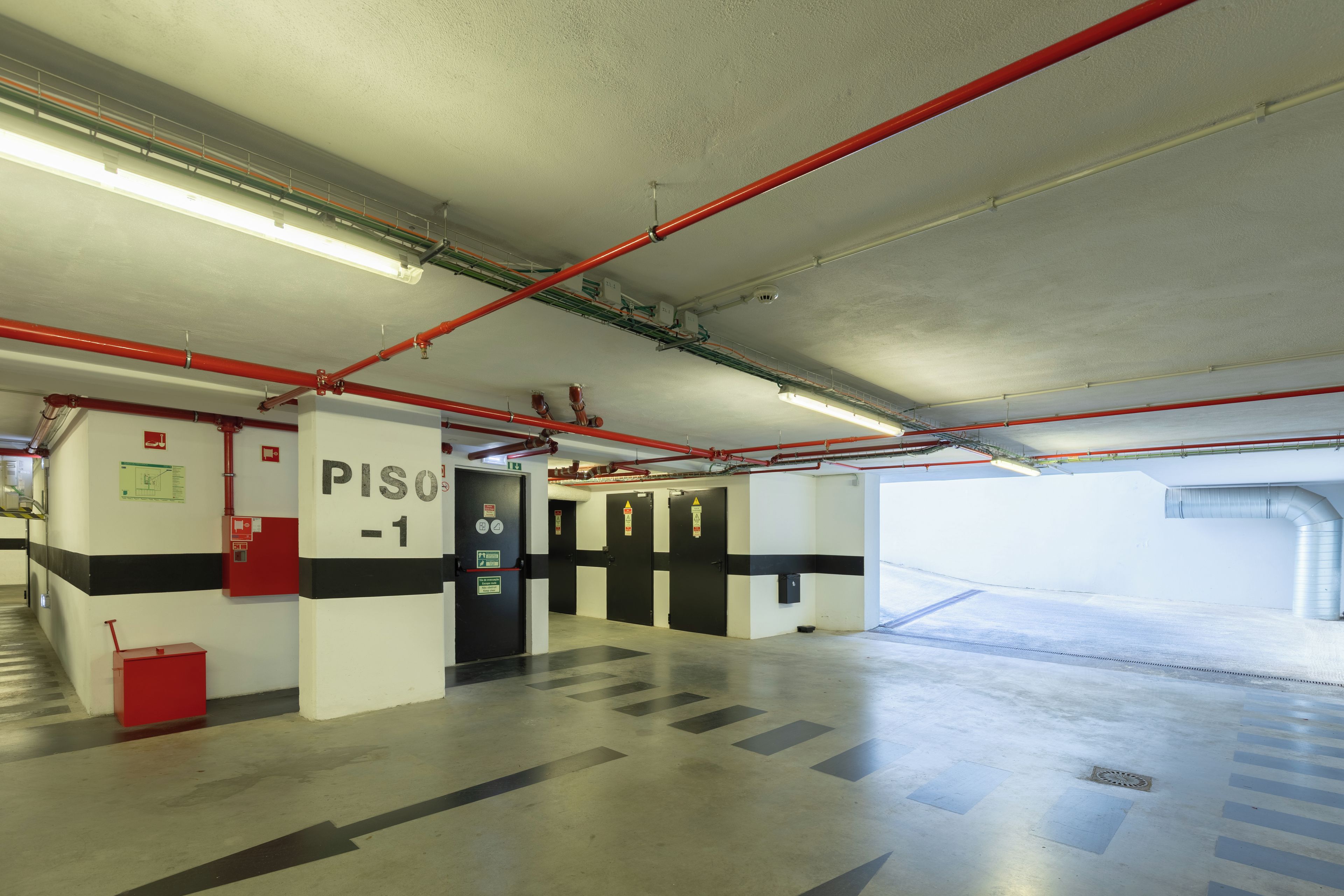 Un estacionamiento con señalización clara, incluyendo una puerta con la inscripción 'PISO -1' y equipo de emergencia.