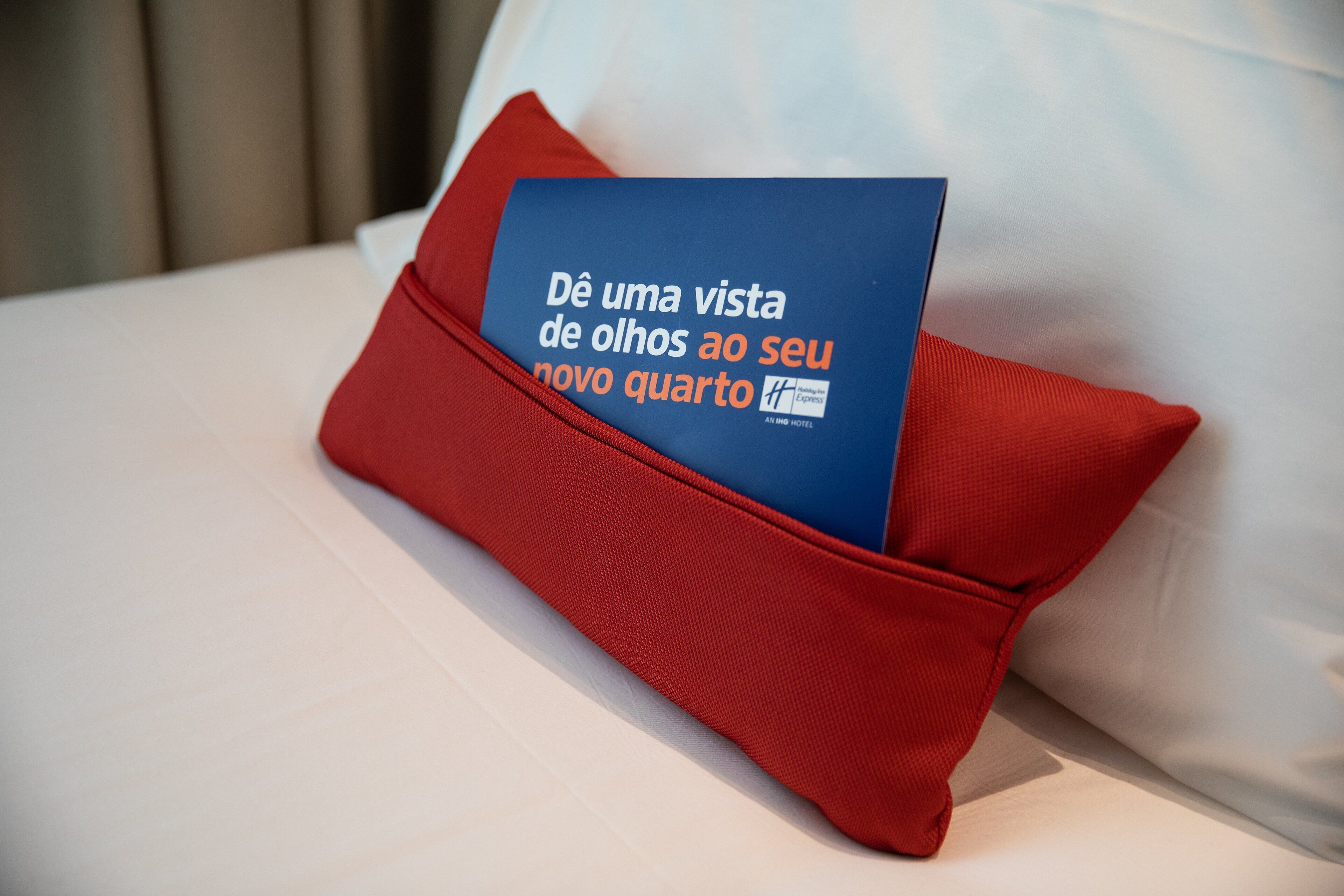 A red pillow with a blue booklet on a white bed.