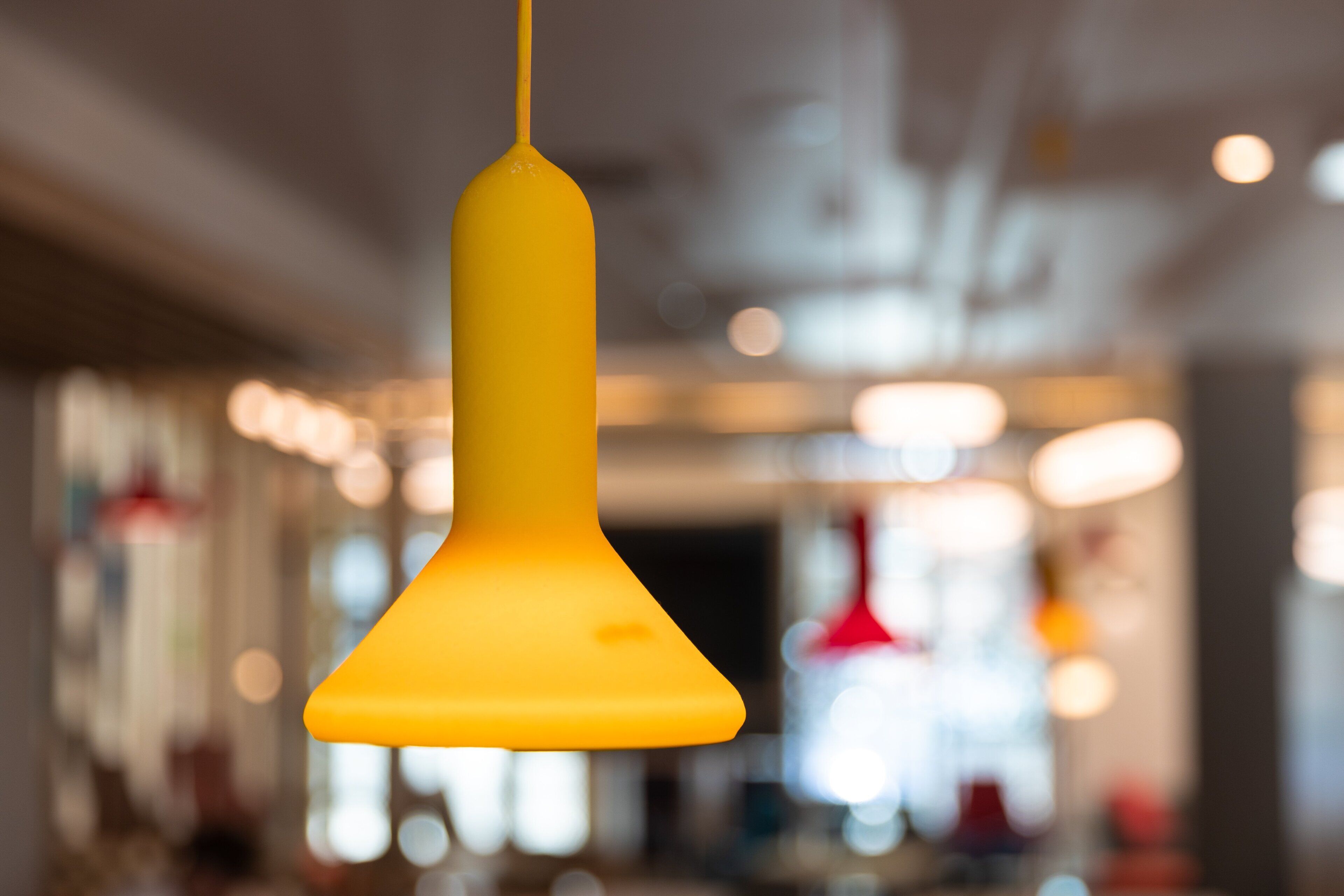 A yellow pendant light fixture in a modern interior space with blurred background elements.