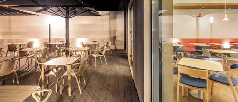 Un comedor interior con mesas y sillas, piso de madera y una pared de vidrio.
