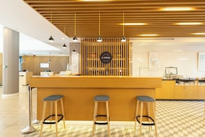 Un café bar con mostrador de madera, tres taburetes y una pizarra con la carta.