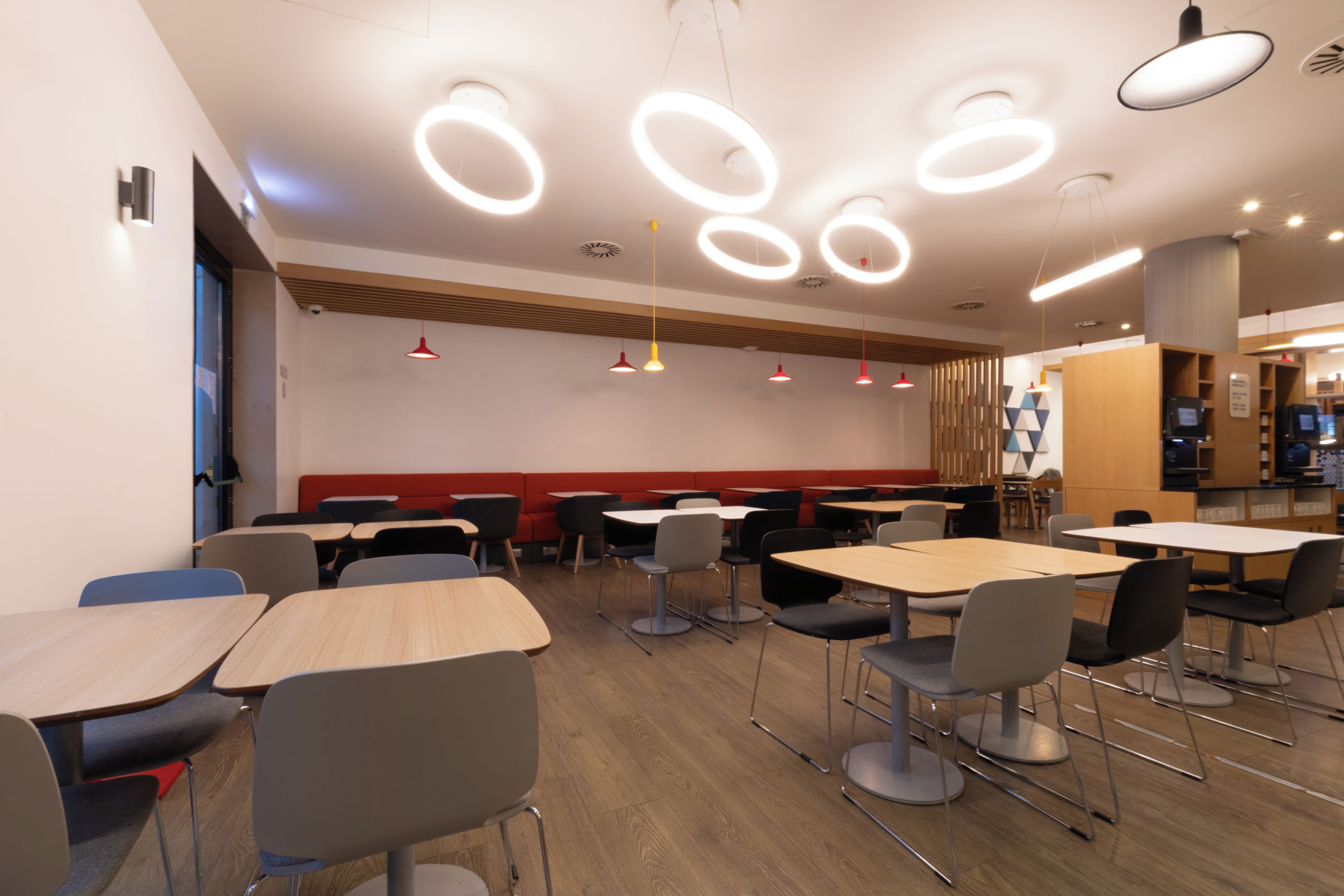 A modern dining area with round ceiling lights, wooden paneling, and a mix of table and booth seating.