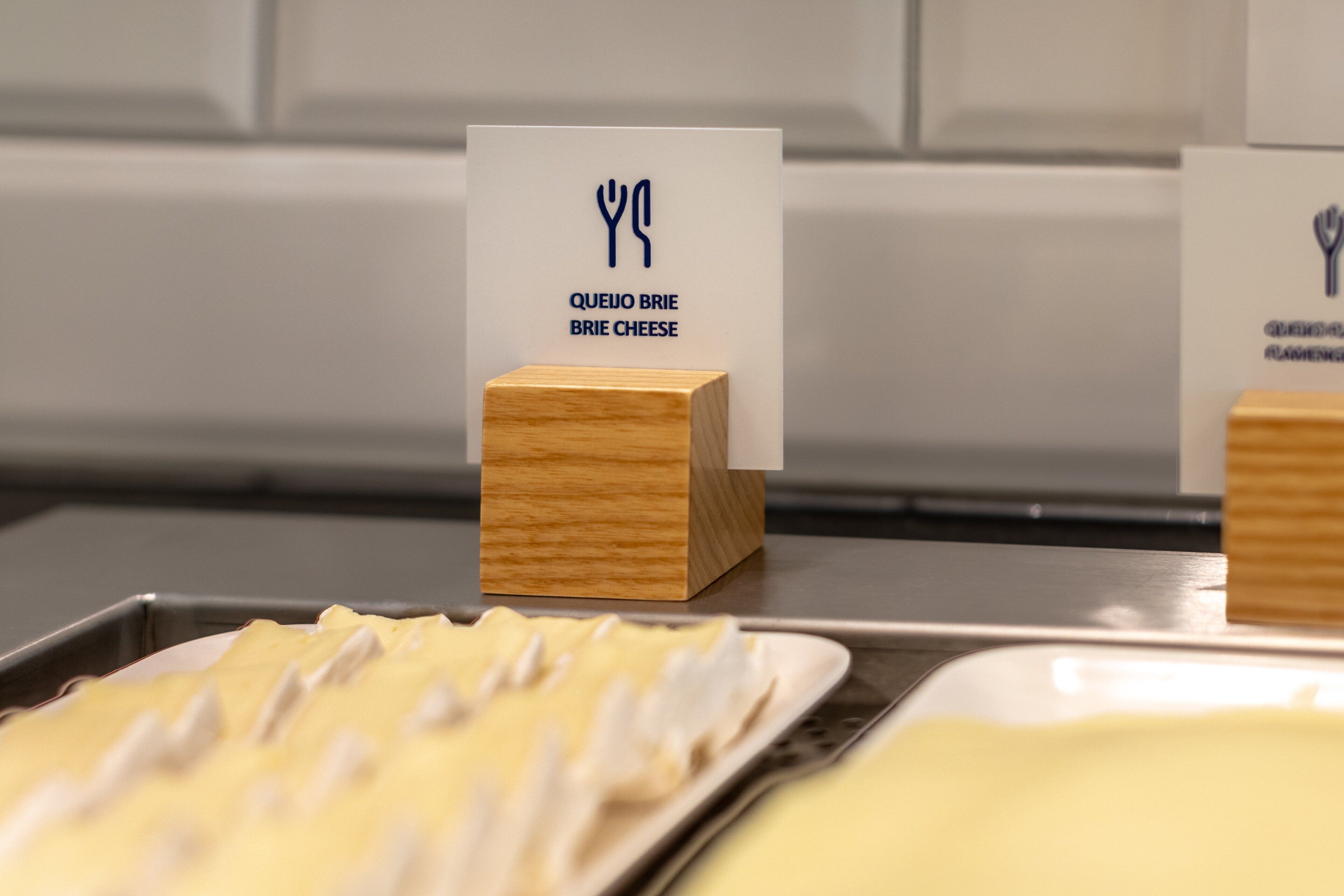 Mostra d'aliments amb un cartell que diu 'Queijo Brie Brie Cheese' i blocs de fusta.