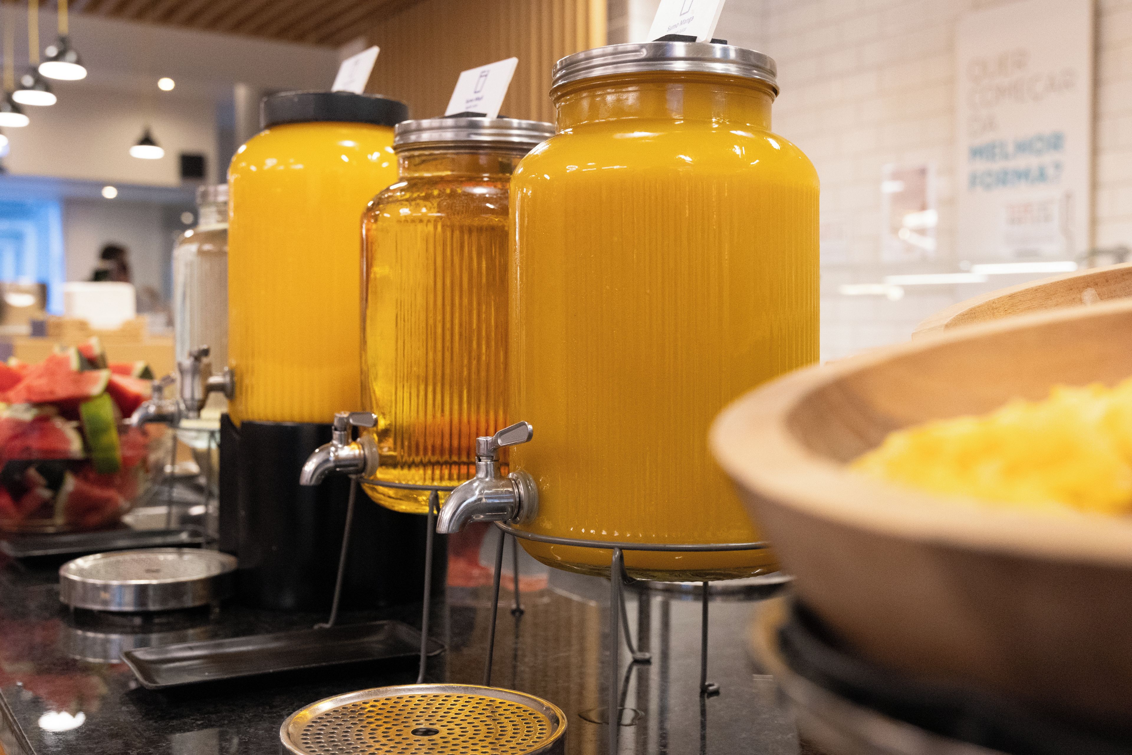 Un bar à jus avec plusieurs distributeurs et un saladier rempli de fruits.