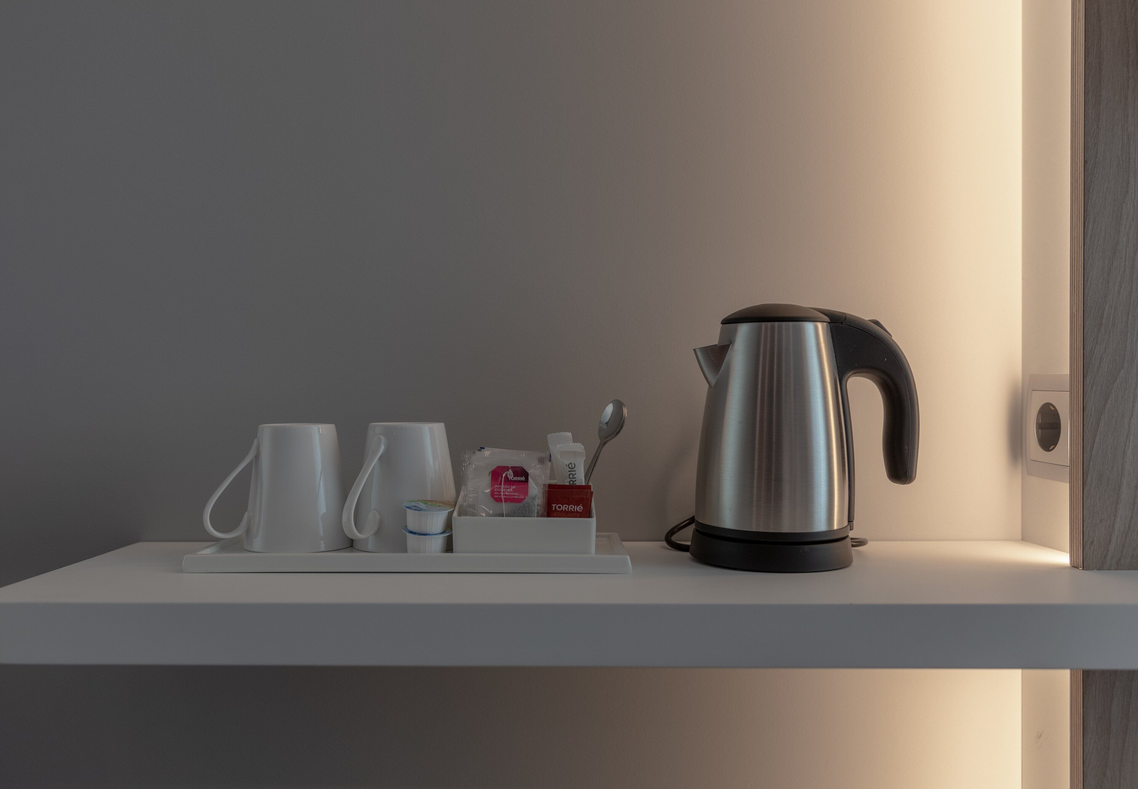 A white shelf with a stainless steel kettle, two white mugs, a small container with a spoon, and a box labeled "TORRIE".