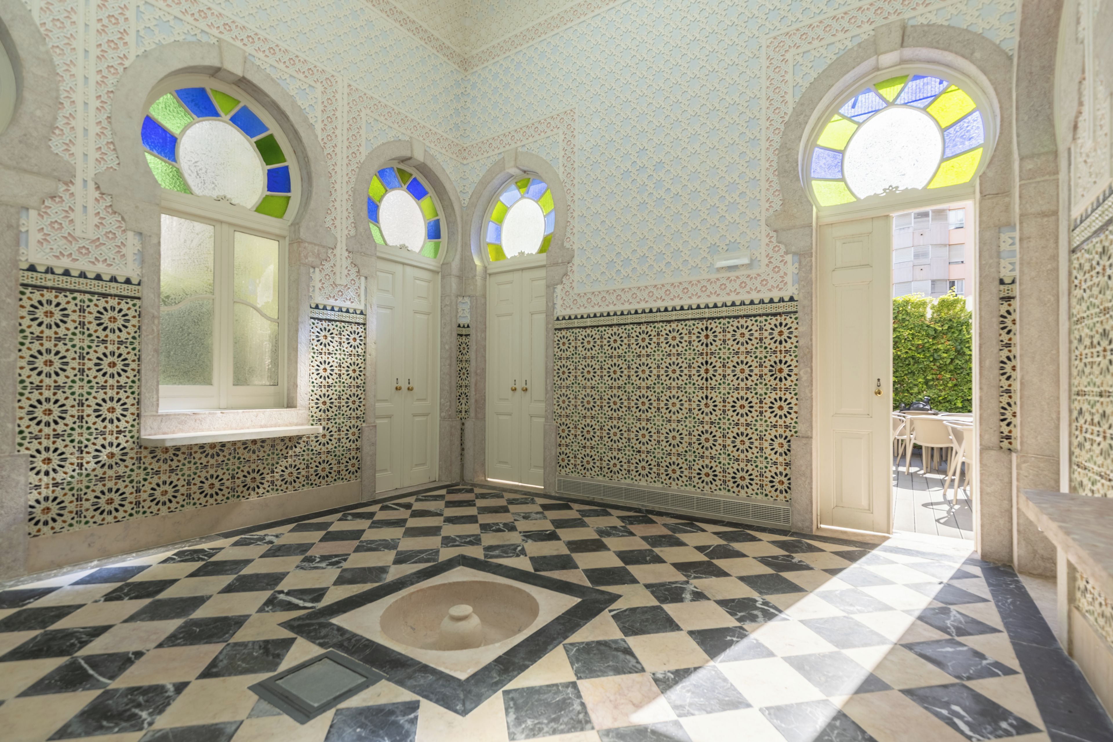 Una habitación con piso a cuadros, ventanas arqueadas con vidrieras y paredes con diseños.