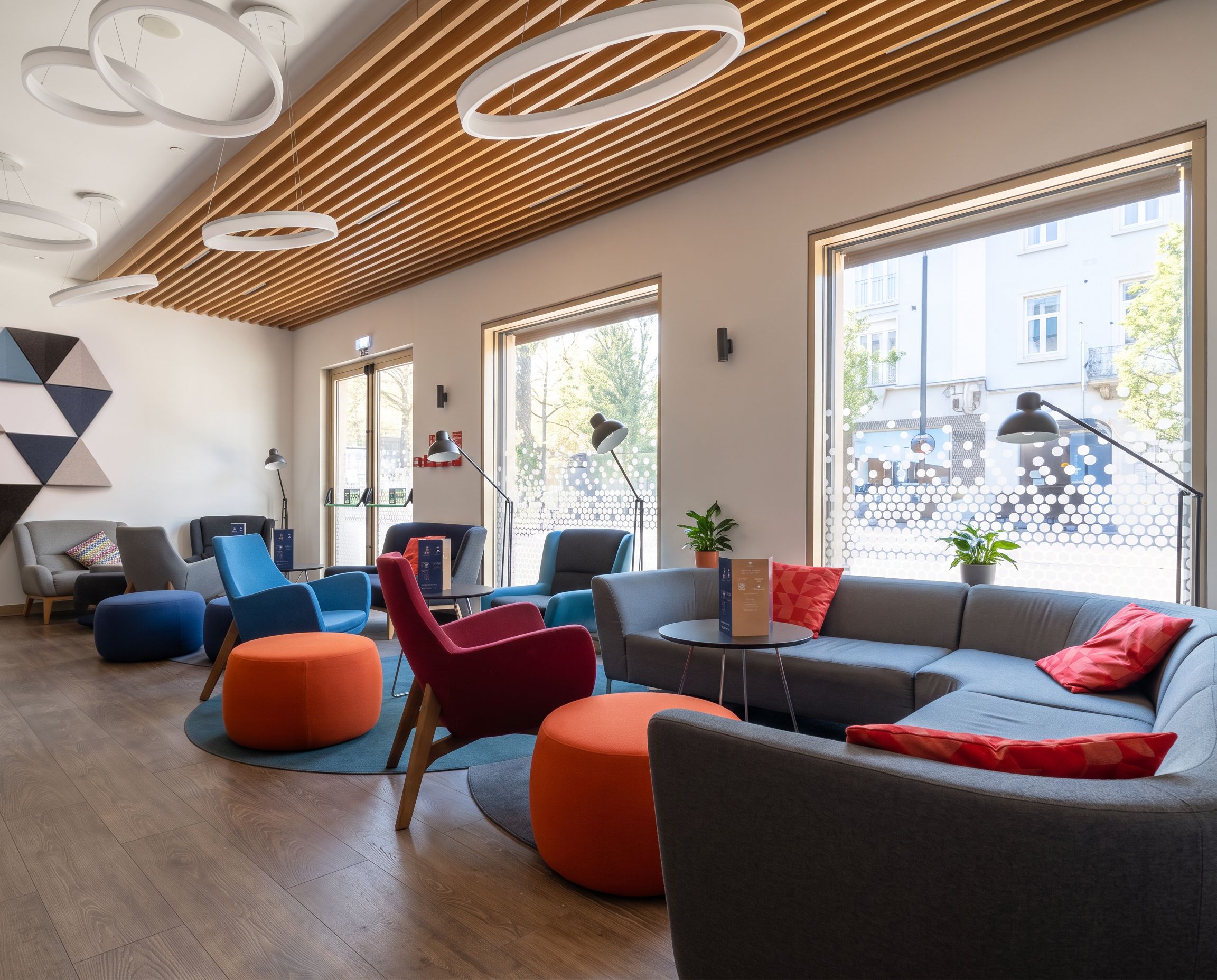 Ein modernes Interieur mit Holzbalkendecke, großen Fenstern und verschiedenen Sitzgelegenheiten, darunter Sofas und Poufs.