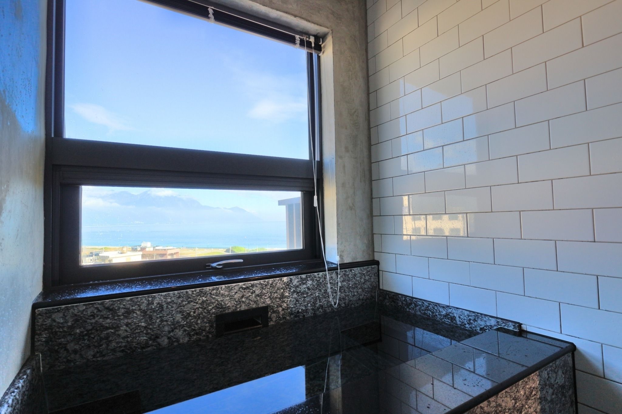 A bathroom with a large window, white tiled walls, and a granite countertop.
