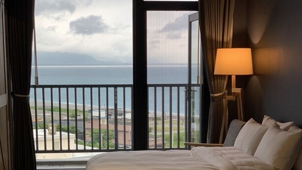 A hotel room with two beds, a view of the sea, and a lamp. - Comesit (Xincheng)