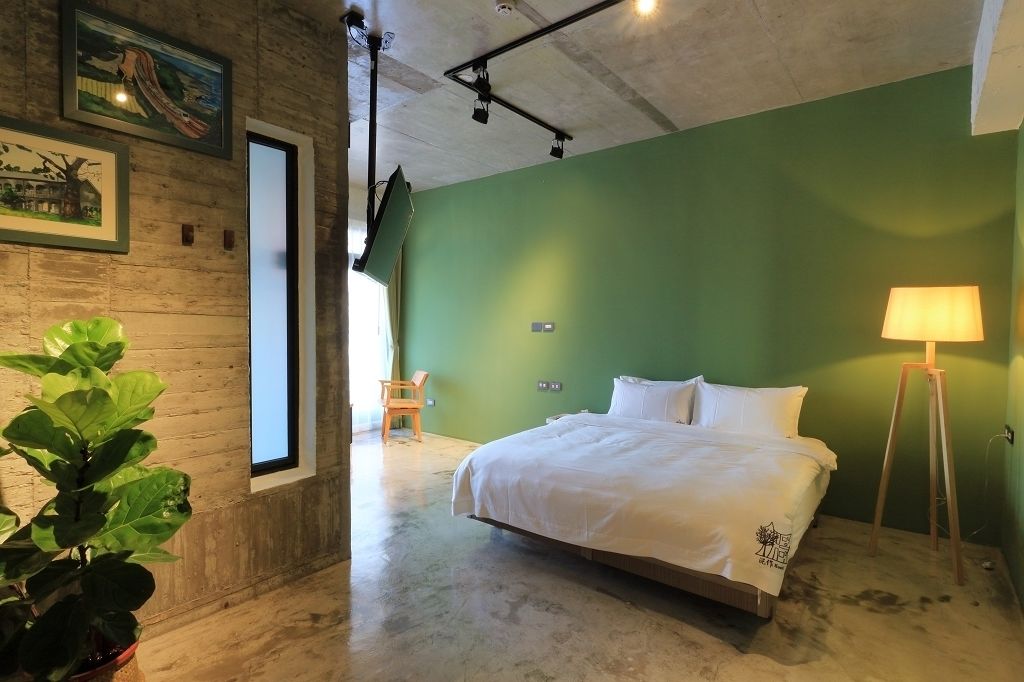 Une pièce avec un lit, un mur vert, un plancher en bois et une plante en pot.