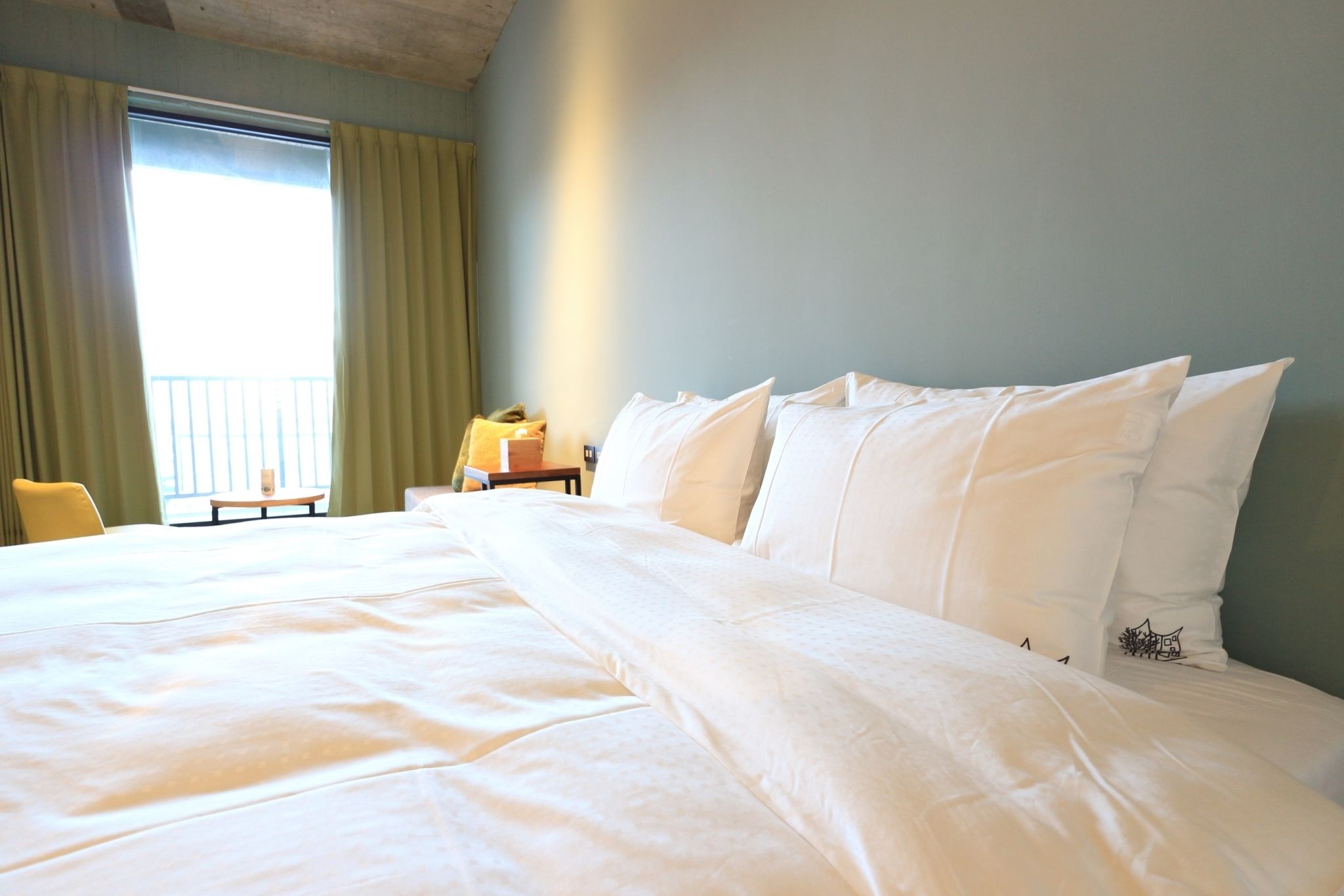 A hotel room with a large bed, a chair, a small table, and a window with curtains.