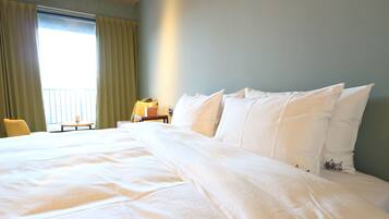 A hotel room with a large bed, a chair, a small table, and a window with curtains.