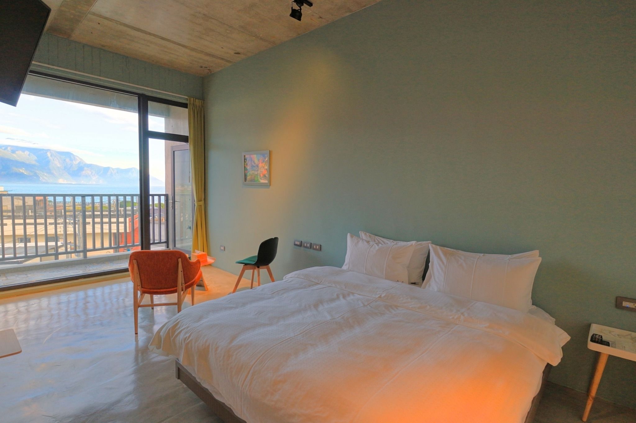 Een slaapkamer met een groot bed, een stoel, een bureau en uitzicht op zee.