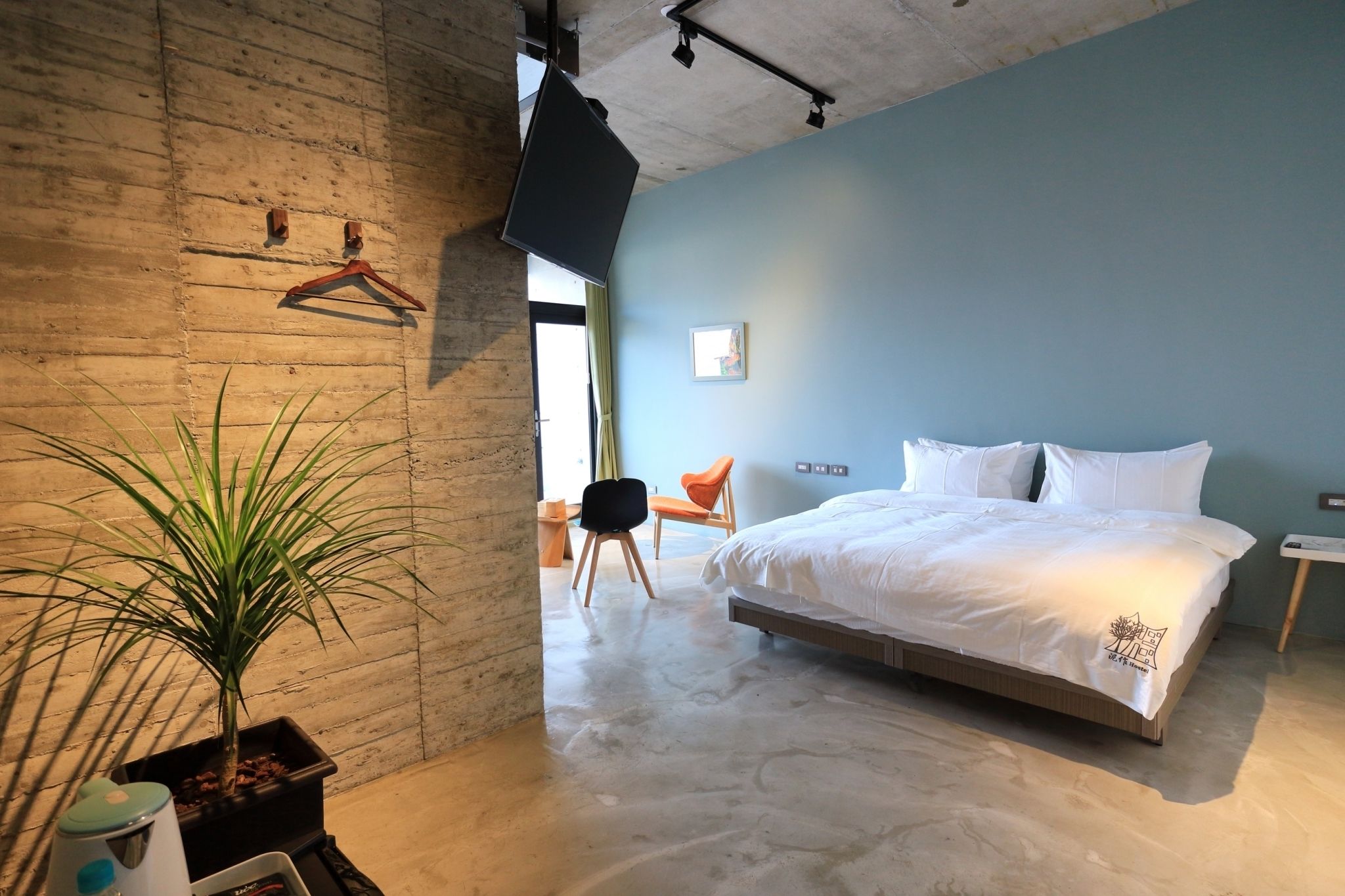 A modern hotel room with a large bed, a potted plant, and a hanging TV.
