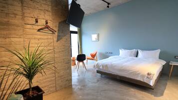 Una habitación de hotel moderna con una cama grande, una planta en maceta y un televisor colgante.