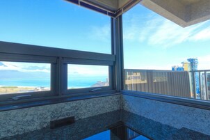 Una habitación con un ventanal grande que da a la costa, incluyendo un cuerpo de agua y montañas a lo lejos.