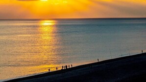 A sunset over a calm sea with silhouettes of people on a beach. - Comesit (Xincheng)