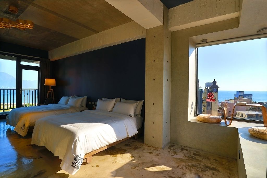A bedroom with two beds, a large window with a view of the sea, and a balcony with a chair.