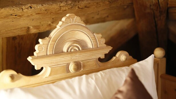 Estructura de cama de madera con detalles tallados y un almohadón.