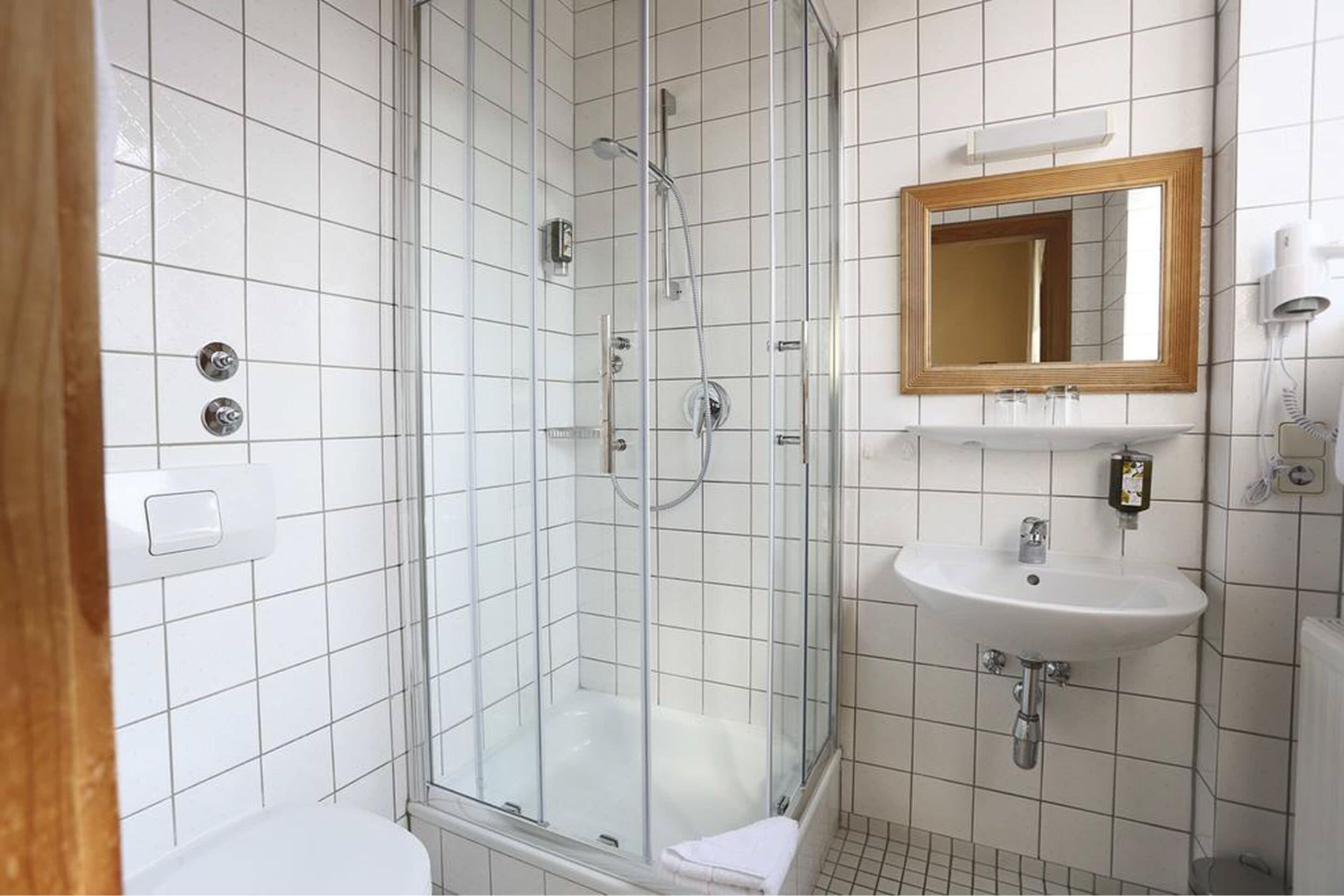 Un baño con ducha envuelta en vidrio, un lavabo blanco y un espejo sobre él.