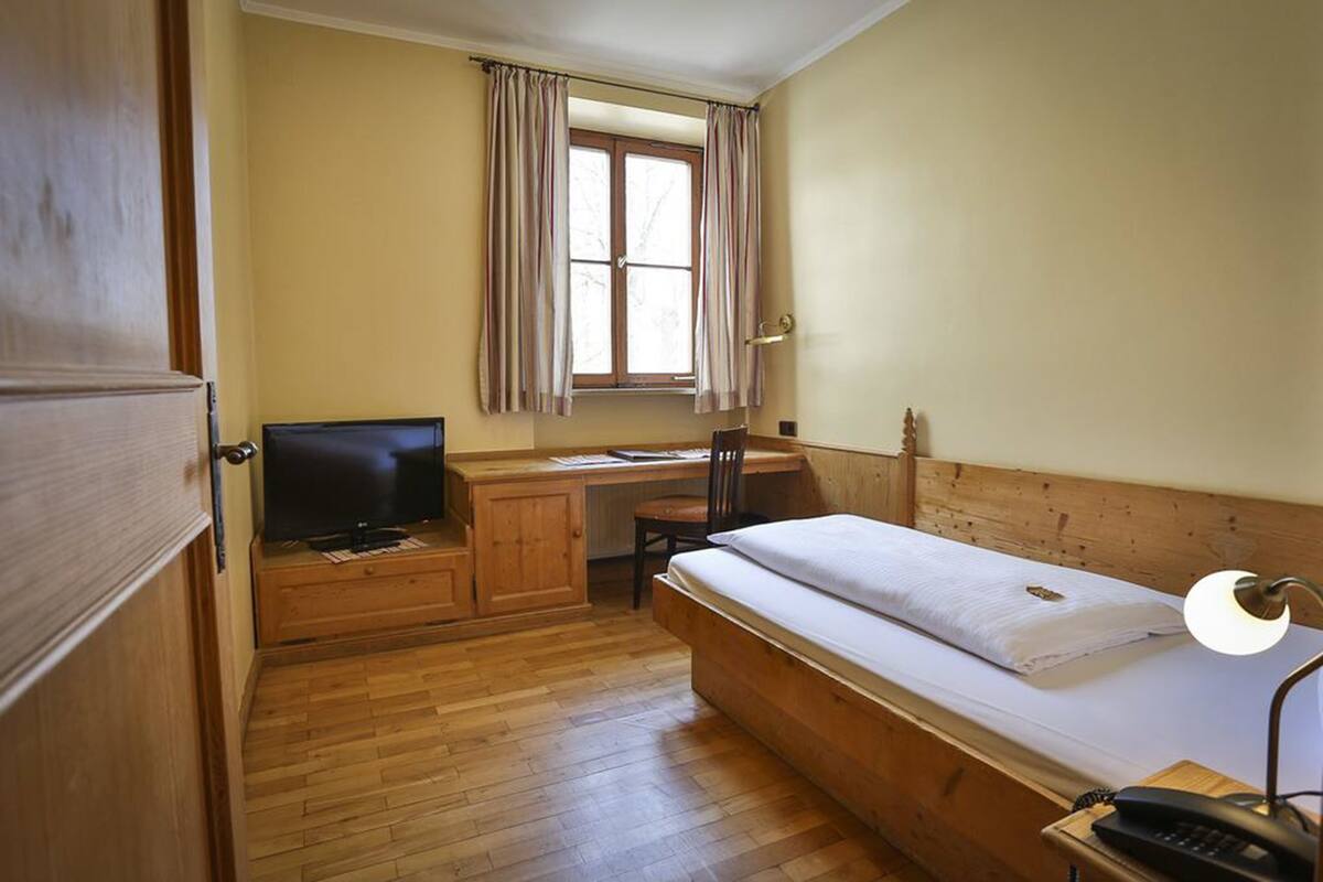 Un dormitorio con una cama de madera, un escritorio con silla, televisor y una ventana con cortinas.