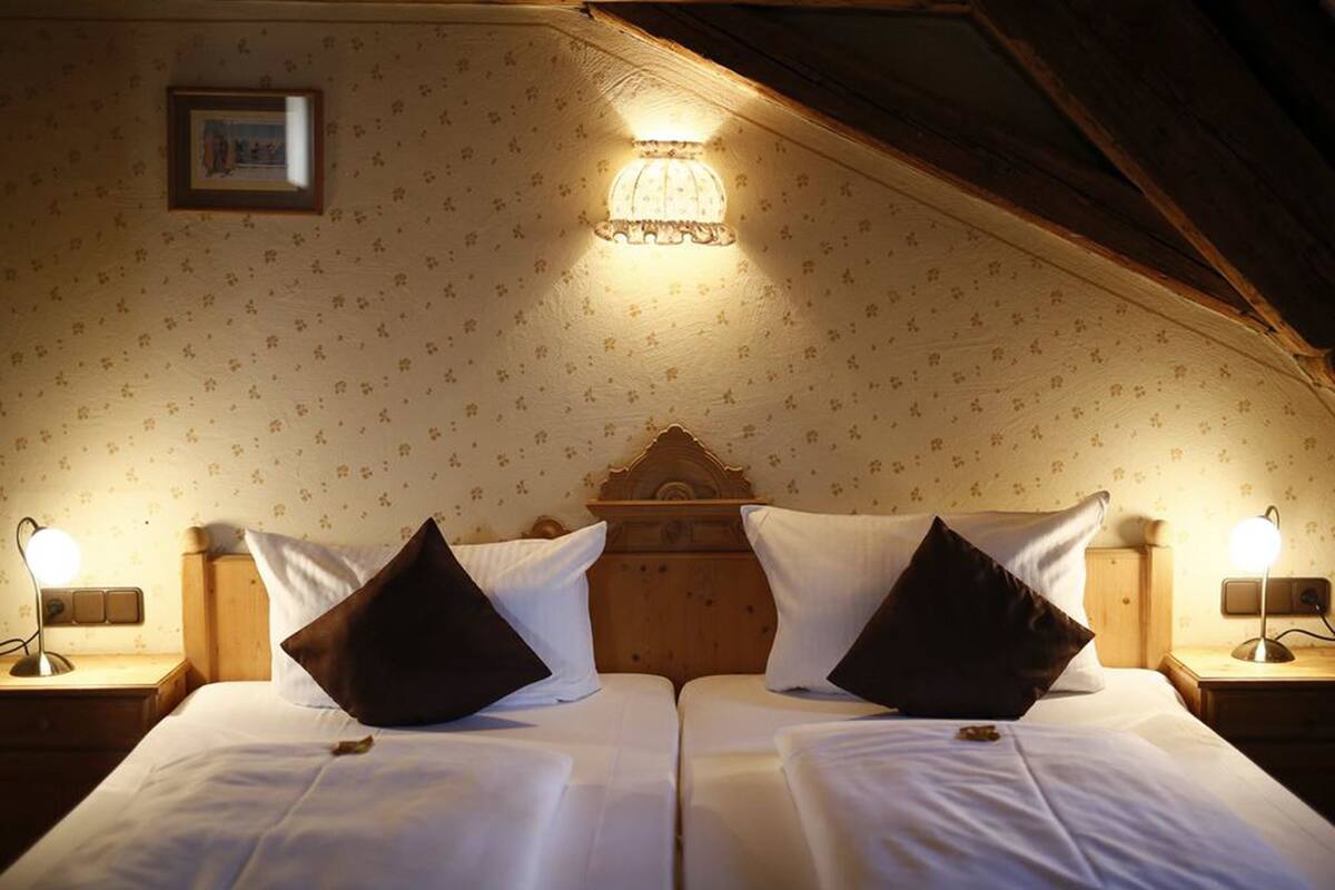 Una cama doble con dos almohadas, un cabecero de madera, una lámpara de pared y un cuadro en la pared.