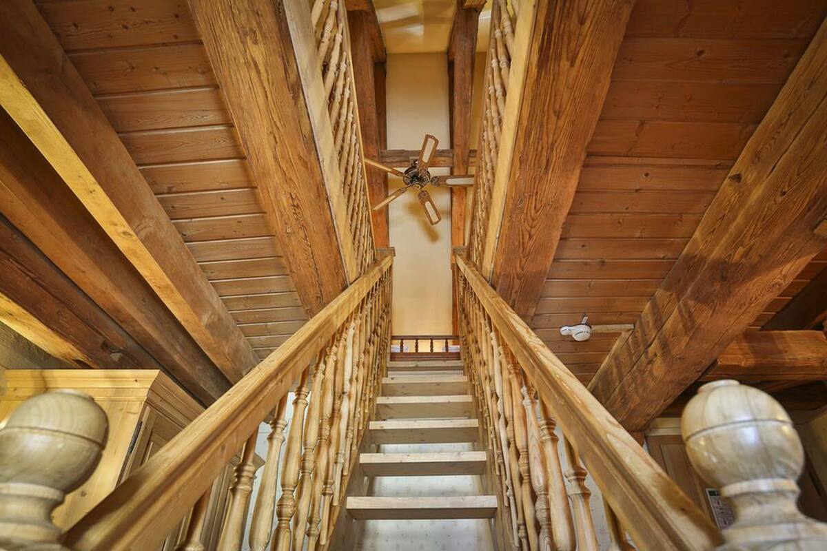 Una escalera de madera con un ventilador de techo, rodeada de vigas y barandillas de madera.