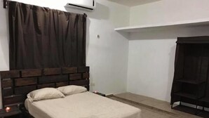 A bedroom with a wooden bed, a nightstand, a wall-mounted air conditioner, and a dark-colored wardrobe. - 330 Hotel Altabrisa (Mérida)