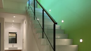 Una escalera moderna con barandillas de vidrio y una pared verde.