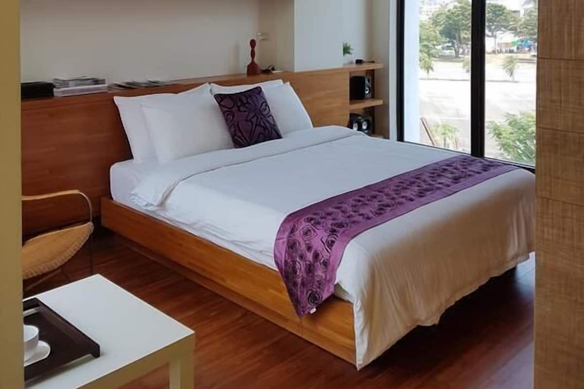 Una camera da letto moderna con un grande letto, una testata in legno, scaffali a muro, un comodino e vista sulla città attraverso ampie finestre.