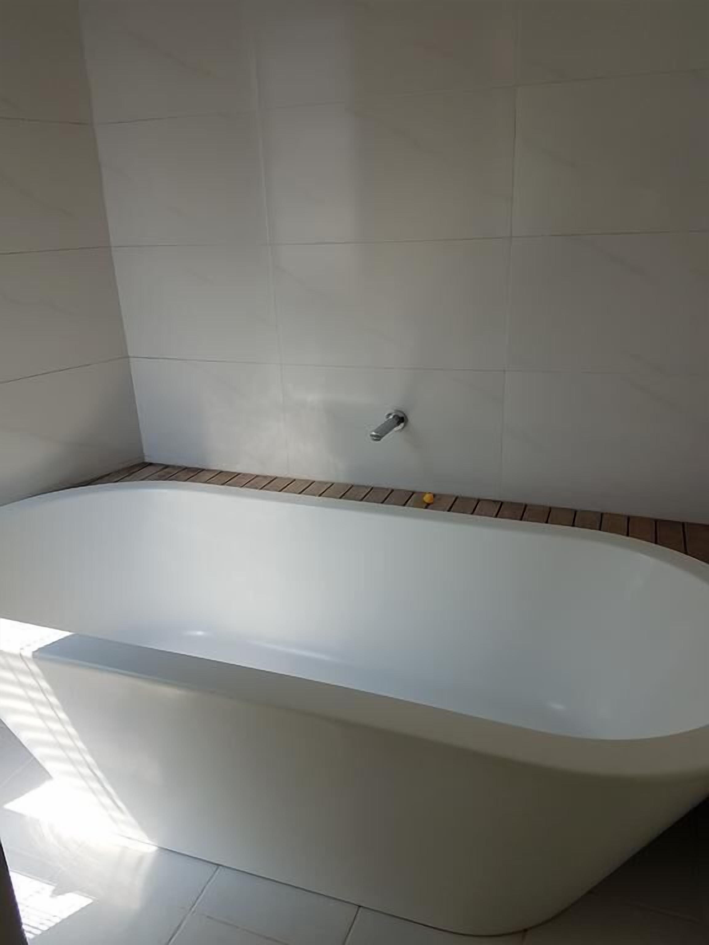 A modern bathroom with a freestanding bathtub, tiled walls, and a wooden floor.