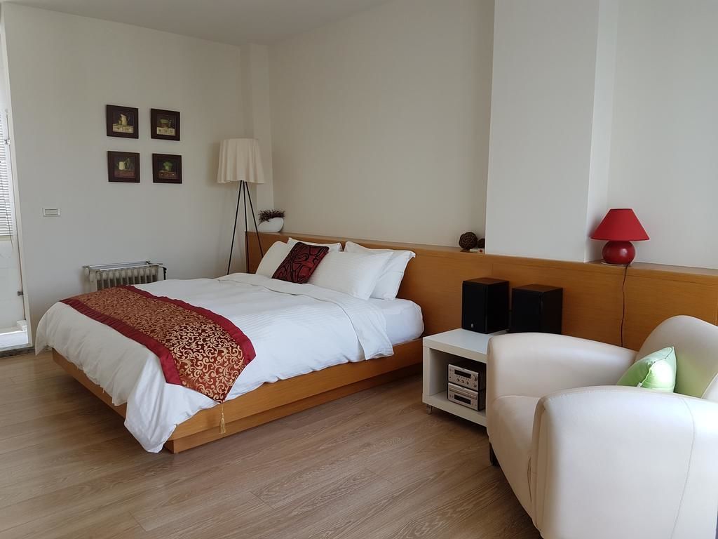 A modern bedroom with a wooden bed, a white sofa, a red lamp, and a small shelf with speakers.