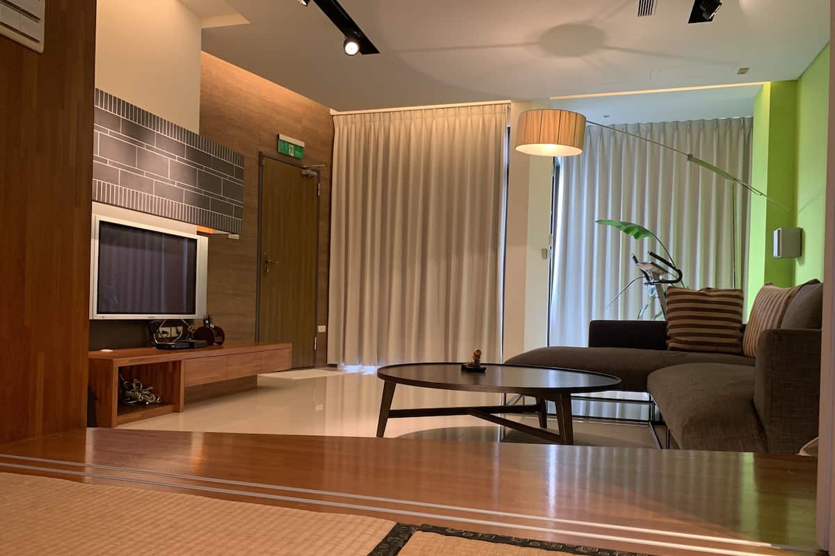 Una moderna camera d'albergo con TV a schermo piatto, una consolle in legno, un tavolino rotondo, un divano e un'ampia finestra con tende.