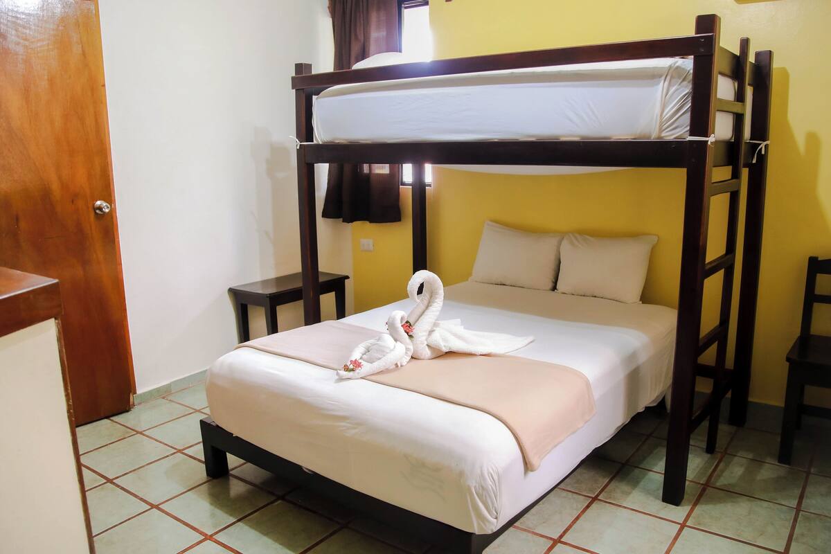 A bunk bed with a swan towel decoration, a bedside table, and a small chair.