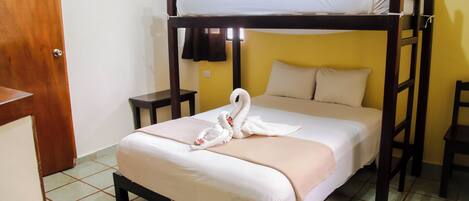 Uma cama de solteiro com uma toalha decorada com cisne, uma mesinha de cabeceira e uma cadeira pequena.